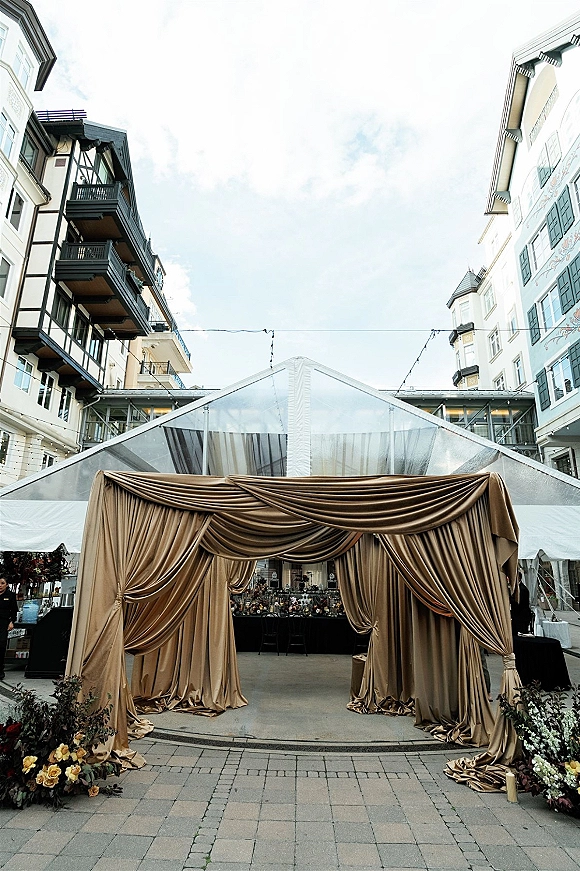 Wedding entrance decor with draped wedding entrance fabric, string lights, and floral greenery framing a clear tent in a hotel courtyard walkway