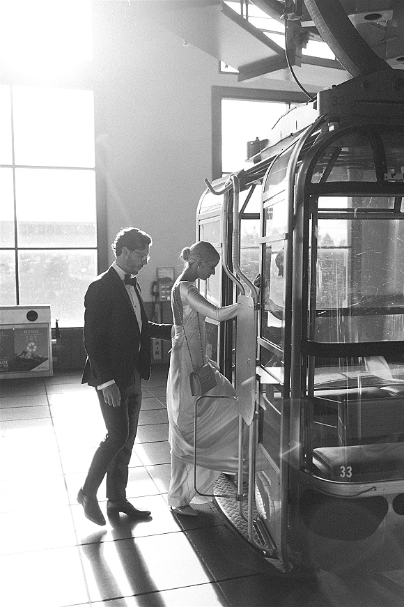 Couple portrait on a tram, bride in a sleek wedding dress with clutch and groom in tuxedo, sunlight streaming through station windows