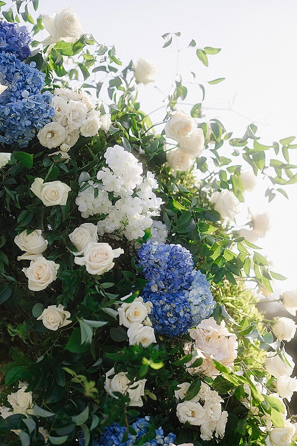 Wedding floral arrangement of blue and white wedding flowers with white roses and hydrangeas, lit by sunlight against a bright sky