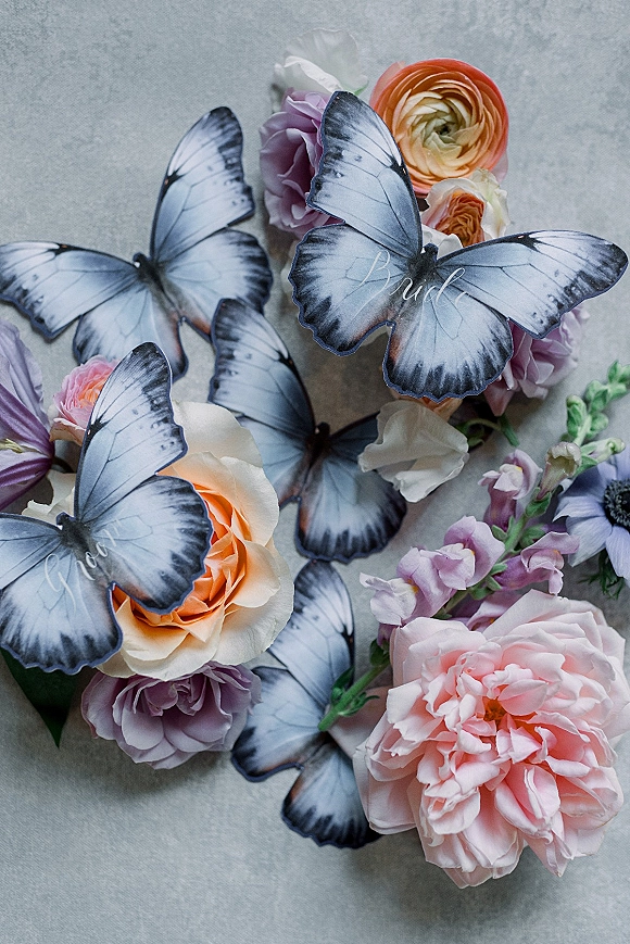 Wedding flat lay with wedding invitation flat lay stationery surrounded by pastel roses and ranunculus on a gray stone surface, butterfly accents
