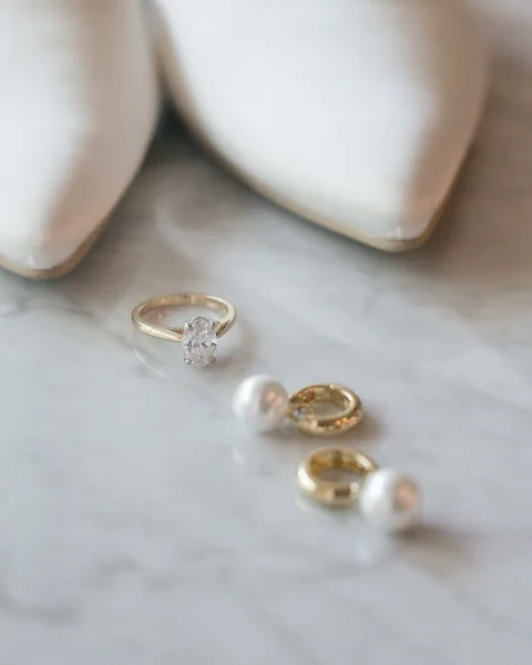Wedding rings and engagement ring close up featuring a diamond solitaire with gold bands on marble, scattered with white flower petals