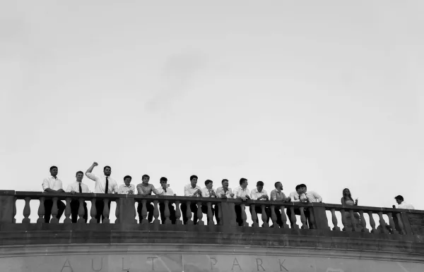 Groomsmen portrait of friends in dress shirts and ties lined up on a stone balcony, leaning on the balustrade with open sky behind