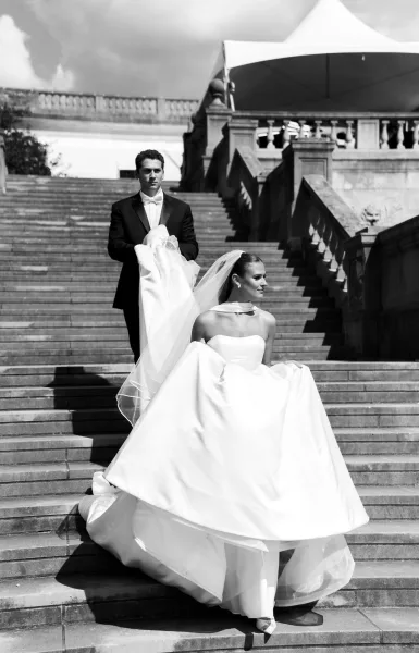 Couple portrait in a black and white wedding portrait style, bride in strapless gown with long veil beside groom in tux on stone stairs