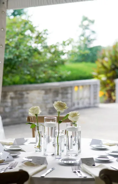 Reception tablescape with a wedding table centerpiece of white roses in glass cylinders and floating candles on an outdoor patio terrace