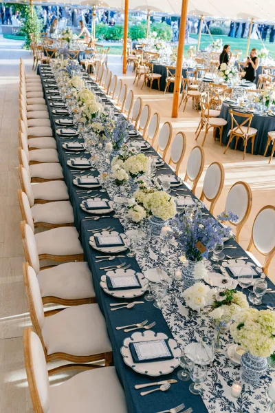 Reception tablescape with navy tablecloth on a long banquet table, chinoiserie vases and hydrangeas under a tented lawn reception with guests