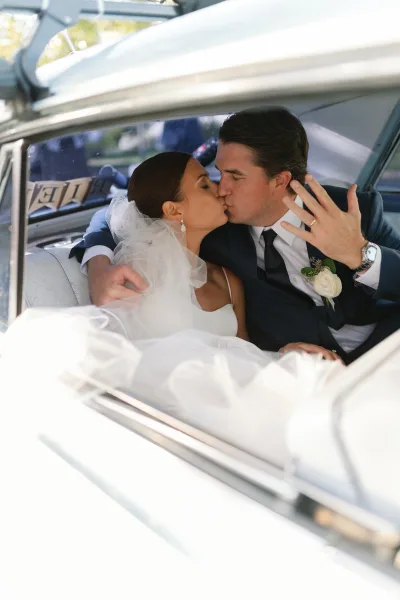 Wedding kiss portrait of newlyweds in car, bride lifting her hand to show the wedding ring as they kiss in daylight by the window