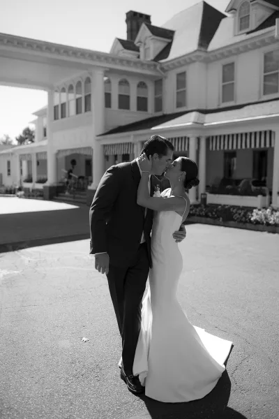 Wedding kiss portrait of bride and groom kissing, bride holding his face in strapless gown beside a large estate house with striped awnings