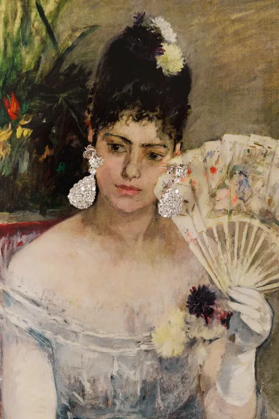 Bridal portrait of a bride in a white dress holding a hand fan, wearing statement earrings, against a painted backdrop with greenery