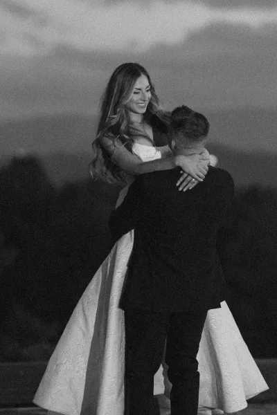 First dance as bride in a strapless gown and groom in a suit embrace closely outdoors beneath a moody night sky landscape