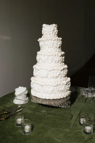 Wedding cake with tiered wedding cake ruffle buttercream on a clear acrylic stand, with votive candles and champagne flutes on green velvet table