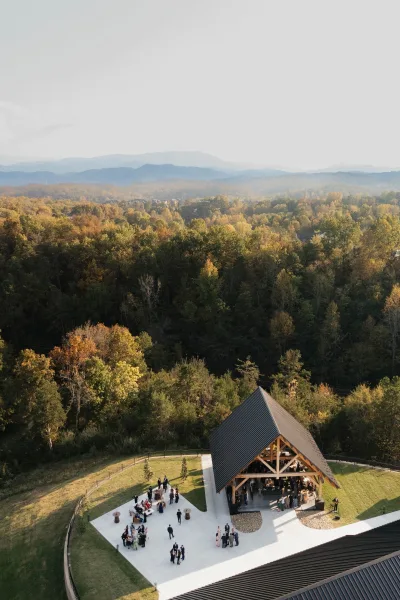 Outdoor wedding reception at an aerial wedding venue with timber-frame open-air pavilion, cocktail tables and lounge seating, mountains behind