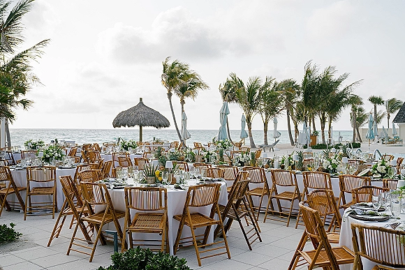 Reception tablescape with white linens, woven placemats, candles, citrus and floral centerpieces on a beachfront patio with palm trees