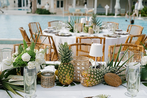 Reception tablescape with tropical wedding tablescape accents, white florals and greenery, pineapples, candles and champagne flutes by a poolside patio
