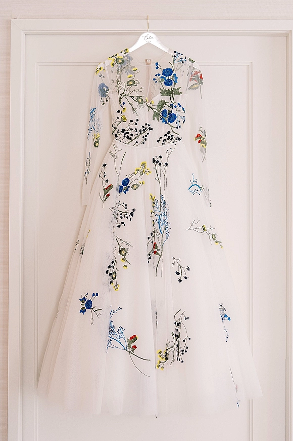 Wedding dress with embroidered wedding dress floral appliques, long sheer sleeves and tulle skirt hanging on a hanger against a white door