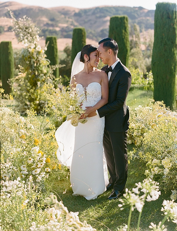 Couple portrait of bride and groom in an outdoor wedding portrait, foreheads touching in a wildflower garden with mountains behind