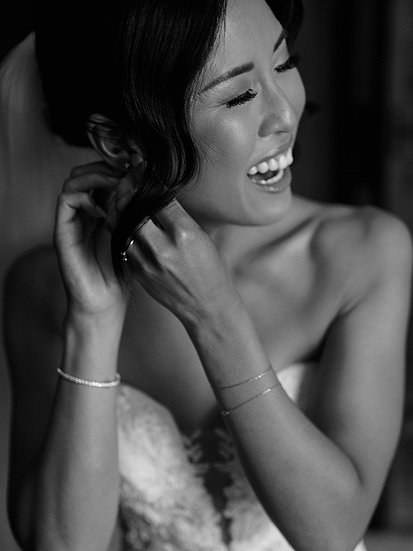 Bride portrait wearing wedding earrings, smiling in a strapless dress with updo and bracelet in a softly blurred indoor room
