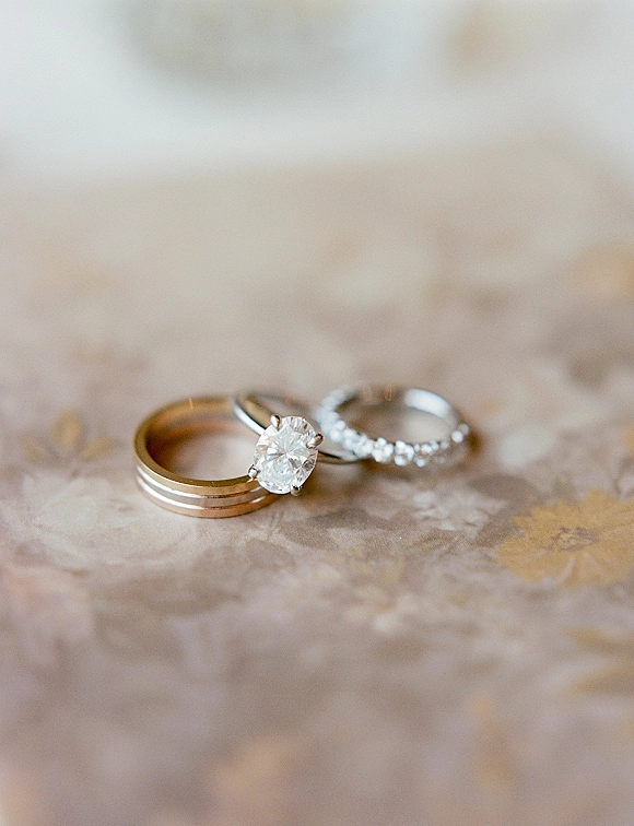 Wedding rings stacked with a diamond engagement ring and gold wedding band on textured neutral paper in a minimal flat lay