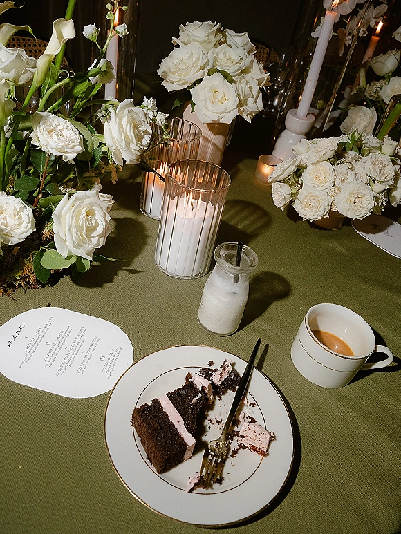 Wedding tablescape with white rose centerpiece and calla lilies, taper candles, and a cake slice place setting on an olive green tablecloth