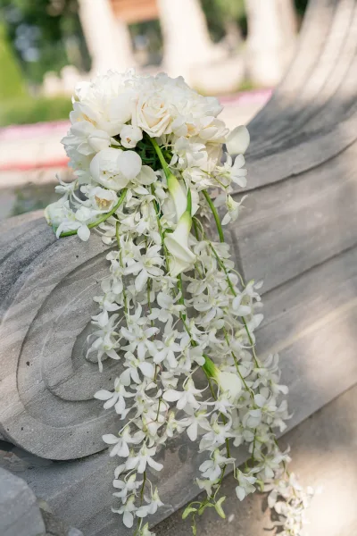 Bridal bouquet with cascading bridal bouquet of white roses, calla lilies, and trailing orchids on a stone bench amid greenery