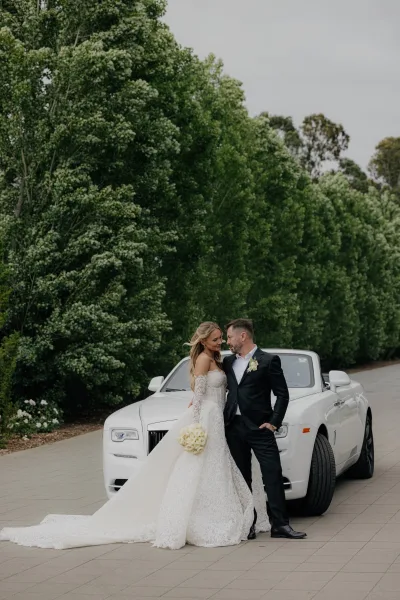 Couple portrait of a bride and groom by car, embracing beside a white convertible, sharing a quiet, romantic moment.
