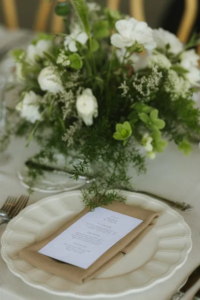 Wedding menu card set as a menu on plate at a refined place setting, accented by a delicate floral centerpiece.