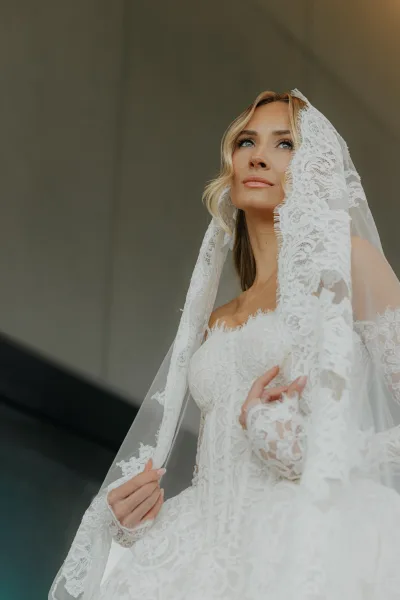 Bridal portrait of a lace veil bride with soft waves hair, gazing serenely as scalloped lace frames her face in a refined, romantic style.