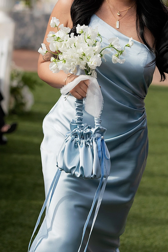 Bridesmaid bouquet of white sweet pea blooms held against a light blue satin dress with chiffon ribbon wrap on a blurred outdoor lawn