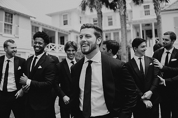 Groomsmen portrait of the groom with groomsmen in suits and neckties, standing by a white house porch with palm trees behind them