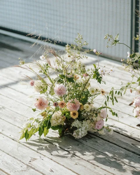 Wedding bouquet with wildflowers and blush-white blooms, airy greenery and grasses on wooden floorboards in soft window light