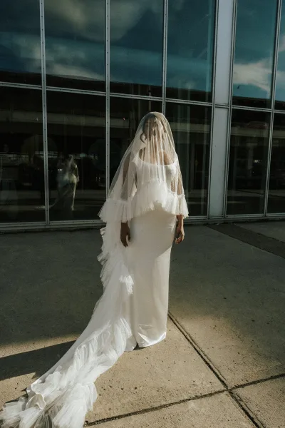 Bridal portrait of a bride in veil with a cathedral veil and long train, walking by a glass building facade with window reflections