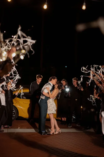 Wedding exit in a ribbon wand send off as newlyweds hurry past cheering guests under string lights against the night sky.