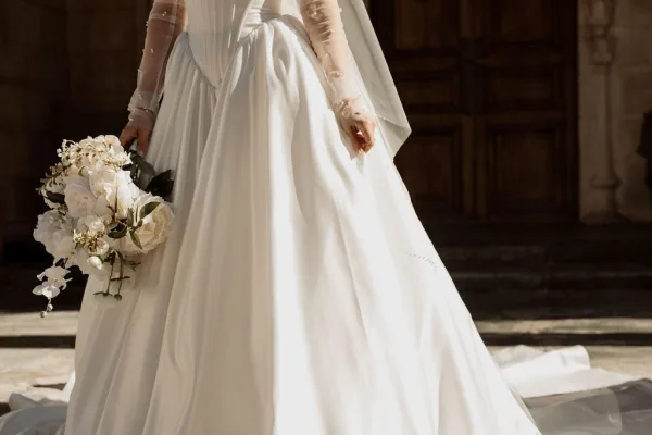 Wedding dress close-up of a long sleeve wedding dress with a corset bodice, framed by rustic wooden doors and worn stone steps.