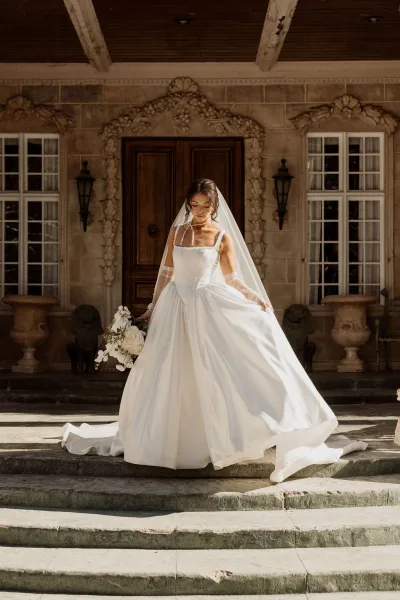 Bridal portrait of a bride holding bouquet on stone steps before a grand wooden door, highlighted by a simple pearl necklace