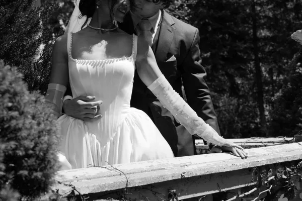 Couple portrait as the bride and groom embrace, her sheer gloves resting on his arm, by an ivy-covered stone railing in a garden