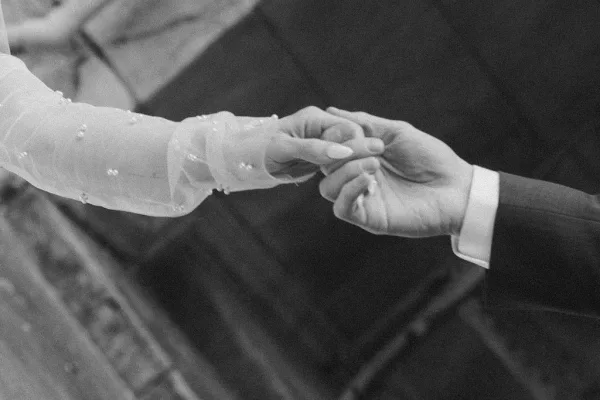 Couple holding hands in a tender wedding handhold detail, her sheer beaded sleeve glinting softly in an intimate close-up.