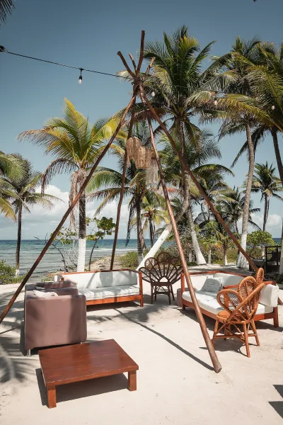 Beach lounge decor with wedding lounge seating, rattan chairs and sofas under string lights, set on sand with palm trees and ocean beyond
