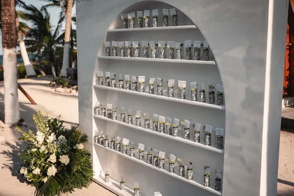Escort card display with patterned cups holding black and white cards, finished with lime accent, on shelves by palm-lined walkway