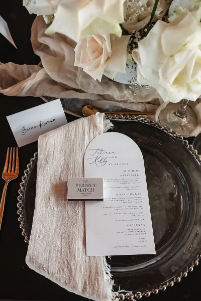 Wedding tablescape with wedding place setting featuring arched menu card, calligraphy place card, beaded charger, copper flatware on dark tabletop