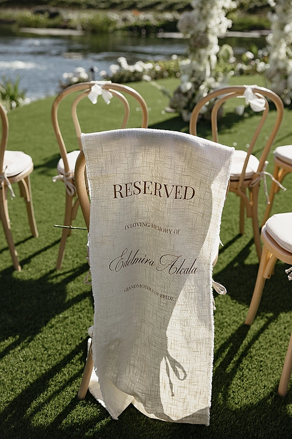 Reserved wedding chair with a linen wedding reserved sign in calligraphy, tied with a white ribbon bow on a bentwood seat by the lawn arch