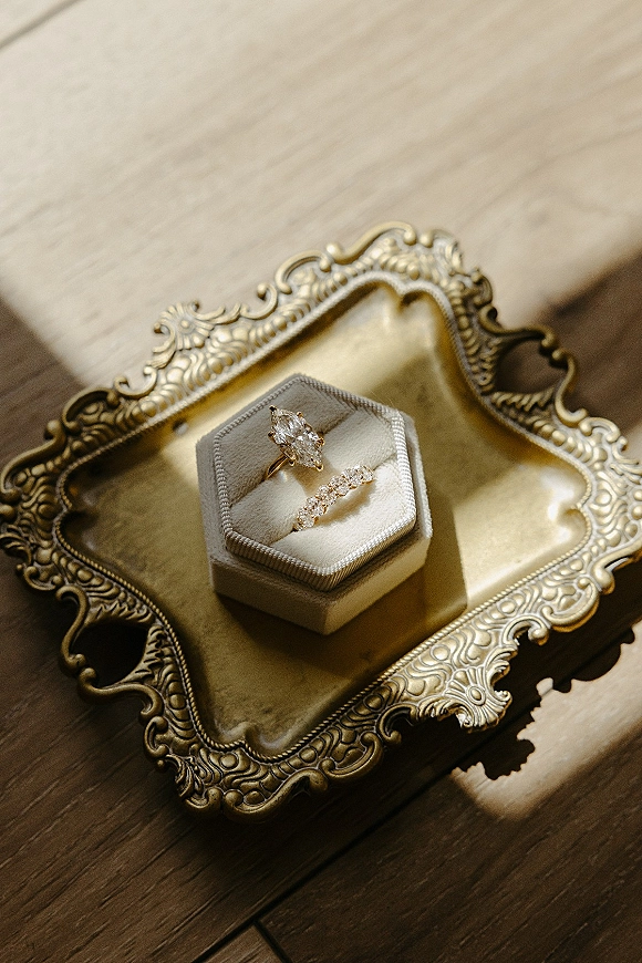 Wedding rings and engagement ring flat lay in a velvet ring box on an ornate gold tray, sunlit on a wood table with shadows