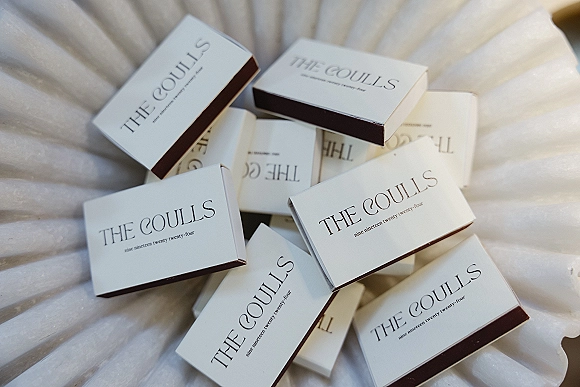 Wedding favors in personalized favor boxes with printed labels and chocolate boxes arranged on white pleated fabric backdrop