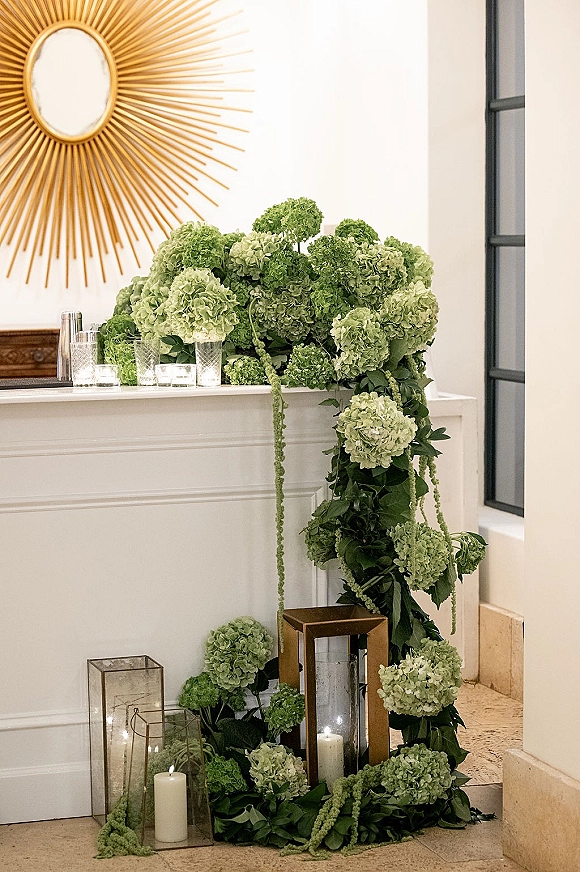 Wedding floral arrangement with green hydrangea wedding flowers and cascading greenery, styled on a white fireplace mantel with lanterns and candles