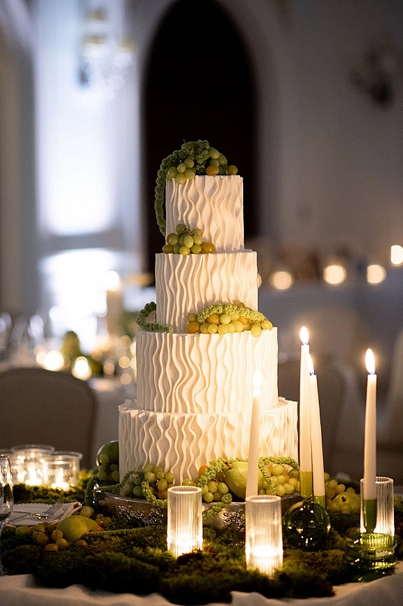 Wedding cake with textured buttercream cake finish, topped with grapes and pears, surrounded by candlelight on a dim reception table