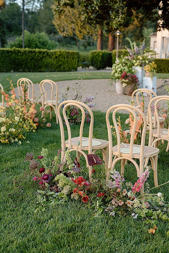 Ceremony aisle decor with a ground floral aisle lining a gravel path, bentwood chairs and greenery garland set on a garden lawn