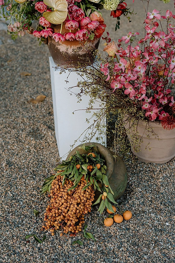 Wedding floral arrangement with ceremony entrance flowers in a terracotta pot atop a white plinth, featuring pink blooms and greenery on gravel ground