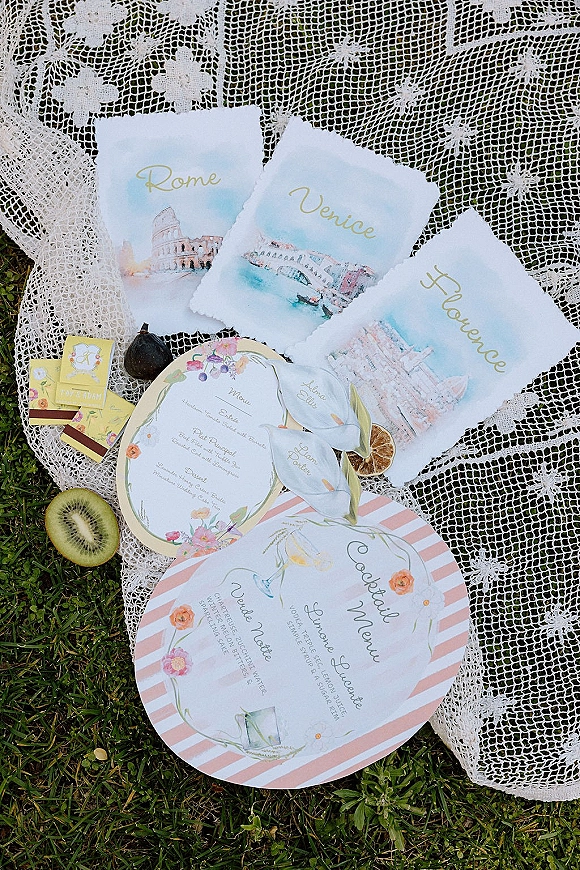 Invitation suite with watercolor wedding invitations on a grass lawn, featuring deckled edge cards, lace cloth, matchboxes, and dried citrus fruit