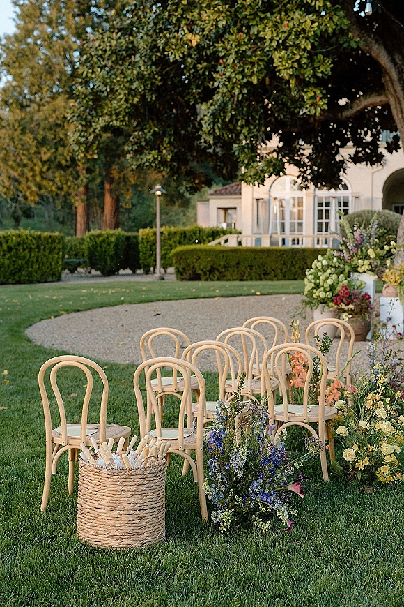 Ceremony seating with outdoor ceremony chairs and bentwood chairs, floral-lined aisle, fan basket, and villa garden lawn backdrop