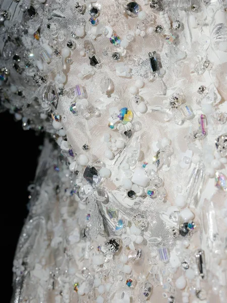 Wedding dress detail with beaded wedding dress crystals and lace appliqué catching light against a dark backdrop, highlighting texture and sparkle