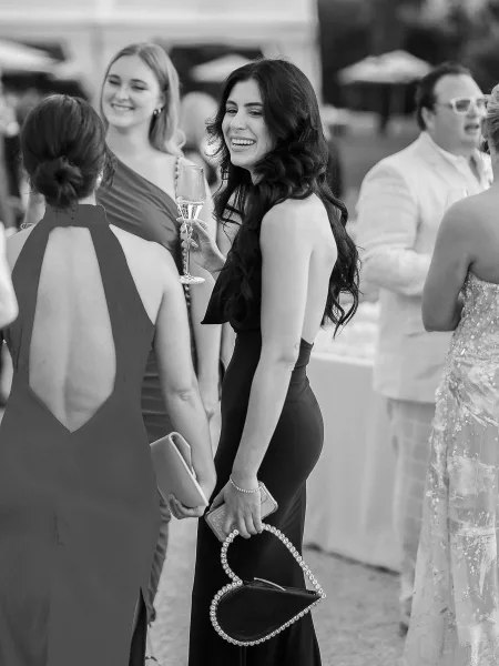 Wedding guest portrait of black tie wedding guests in long black evening gowns holding champagne on an outdoor terrace with umbrellas behind