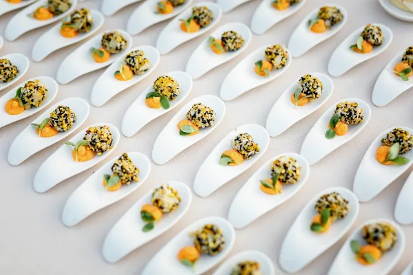 Wedding cocktail appetizers in ceramic tasting spoons, each bite topped with orange puree and microgreens on a linen tablecloth